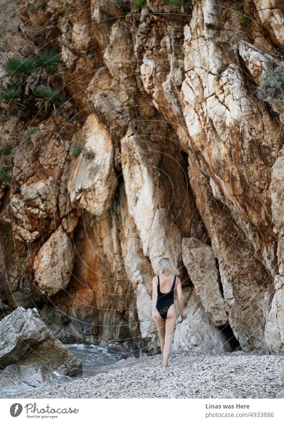 Some pretty moves from a blonde girl in a black swimsuit. Surrounded by rocks and mountains she is on a fine beach. A seaside in Zingaro National Park, Sicily. It’s a place to be on summertime holidays.