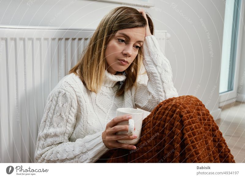 Worried woman sit near heating radiator under blanket with cup of tea gas crisis price rising costs household budget bill calculate home finance worried tax