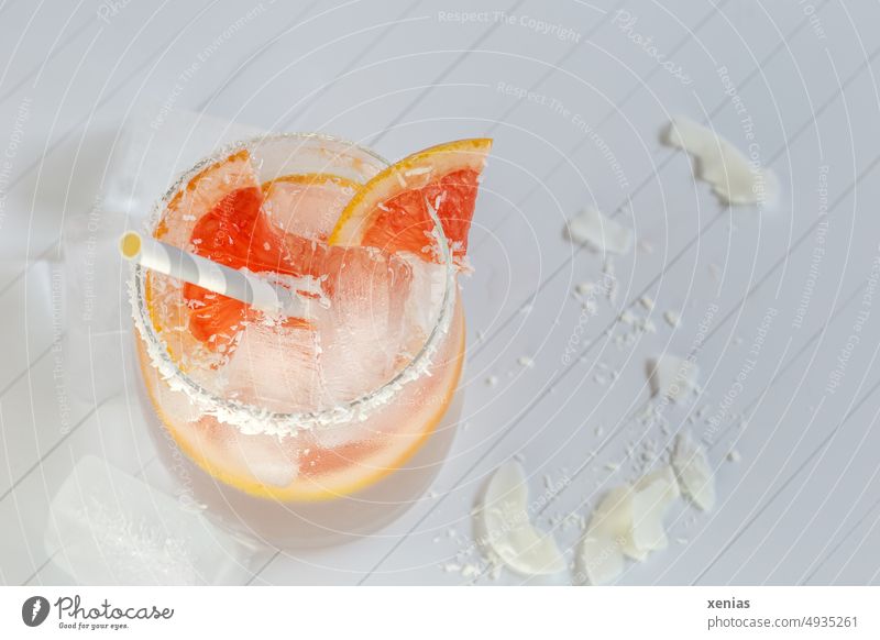 Vitamin water with grapefruit, coconut shavings on the rim of the glass and ice cubes with drinking straw Beverage Cold drink Lemonade Grapefruit Ice cube Straw