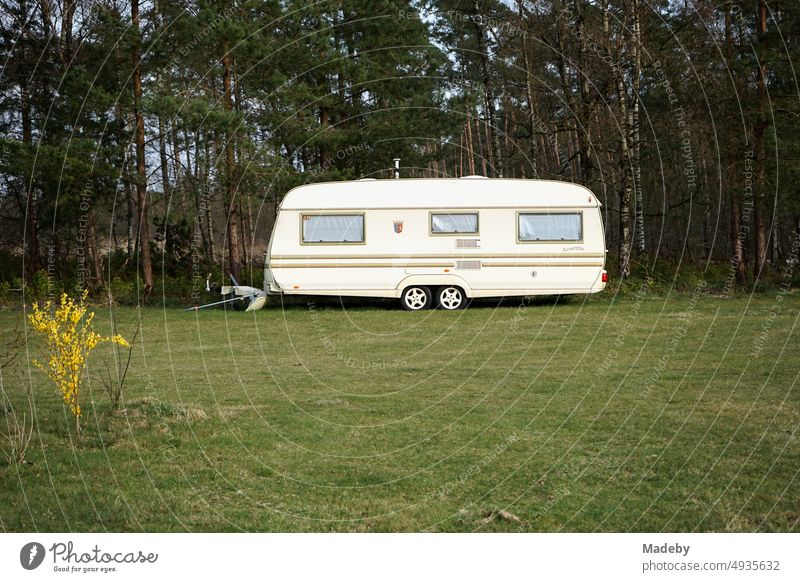 Large caravan in beige and natural colors for camping and vanlife on the campsite in the green with forest and meadow at the glider airfield in Oerlinghausen near Bielefeld on the Hermannsweg in the Teutoburg Forest in East Westphalia-Lippe.