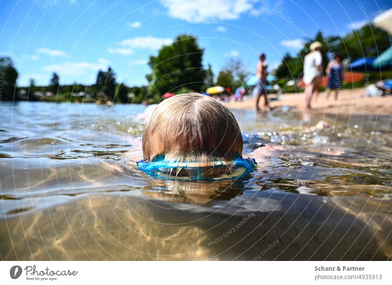 Child with diving goggles dives in swimming lake with bathers on shore vacation Family Blonde Swap be afloat Swimming lake beach holiday family vacation