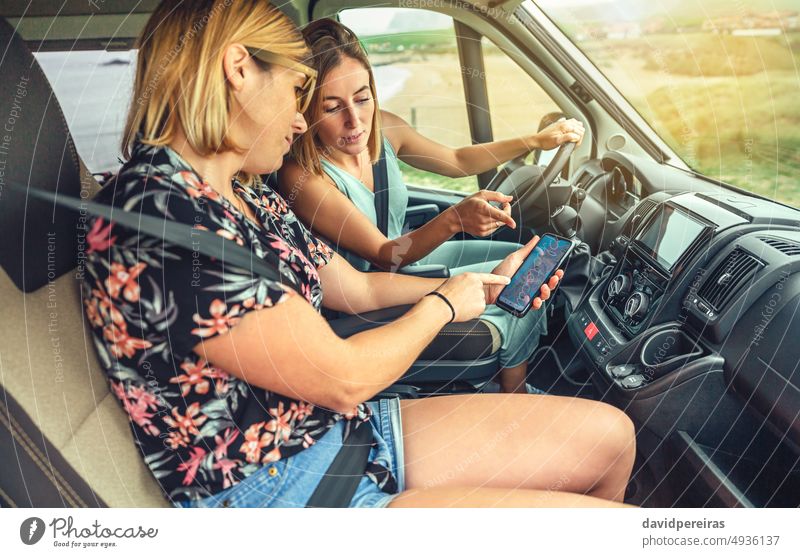 Friends looking gps on the mobile during a campervan trip friend mobile phone travel journey seat belt map vehicle freedom 30s 20s summer person woman