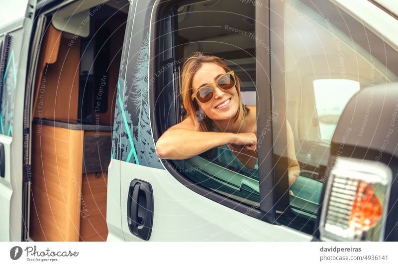 Young woman in sunglasses sitting in camper van leaning on the door happy young summer trip travel smiling journey vehicle freedom 20s person female tourist car