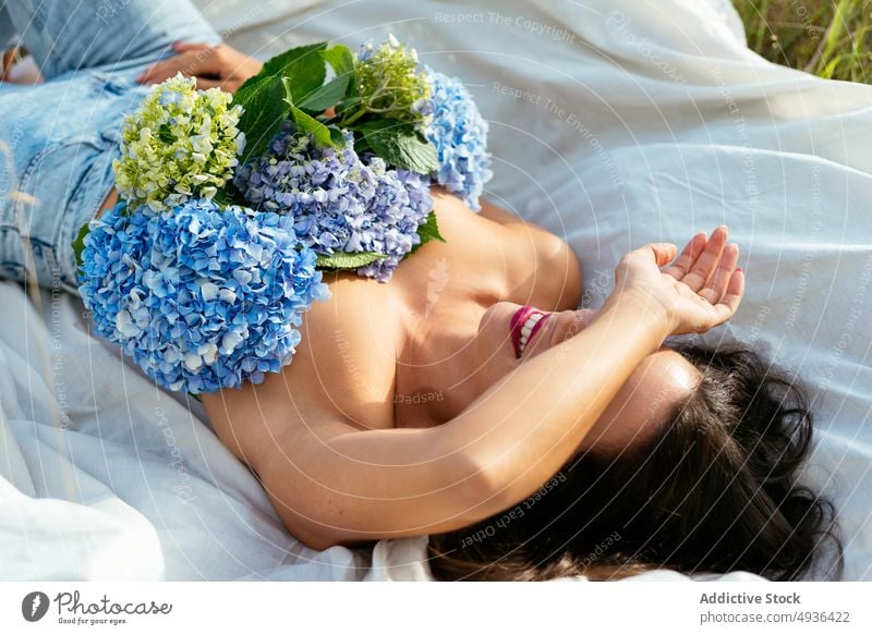 Smiling lady lying on blanket with flowers on naked breast in nature woman smile cover eyes hydrangea allure happy cover breast relax topless female young