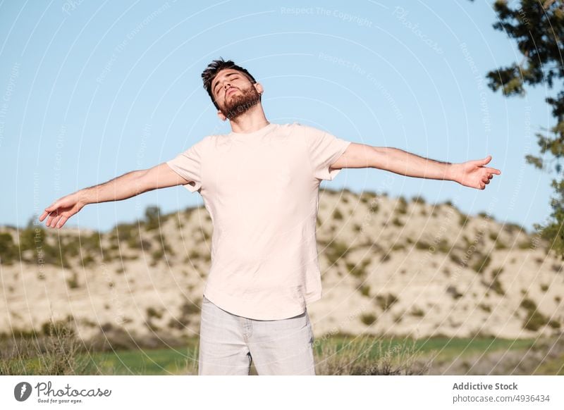 Calm man enjoying freedom in nature calm breathe fresh air countryside hill blue sky spread arms relax male eyes closed young brunet summer peaceful beard
