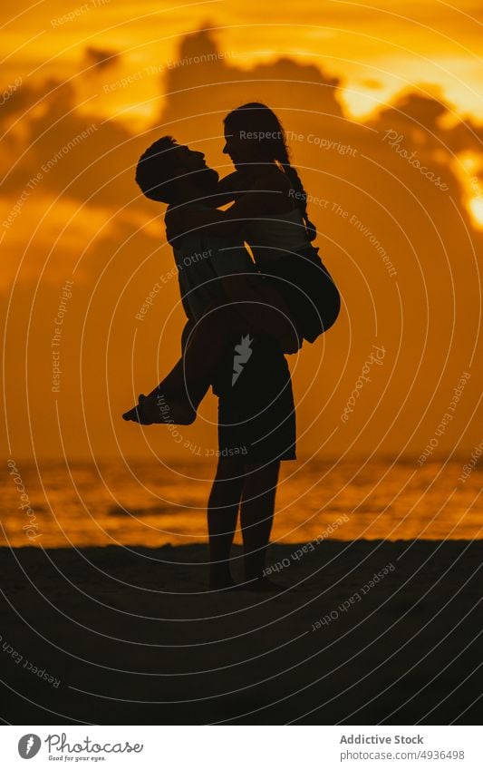 Silhouette of romantic couple embracing and smiling on seashore at sundown embrace beach lift sunset happy love silhouette together hug relationship smile ocean