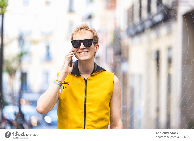Smiling stylish non binary male speaking on smartphone on street man style urban cheerful delight talk transgender phone call confident modern lgbt walk young