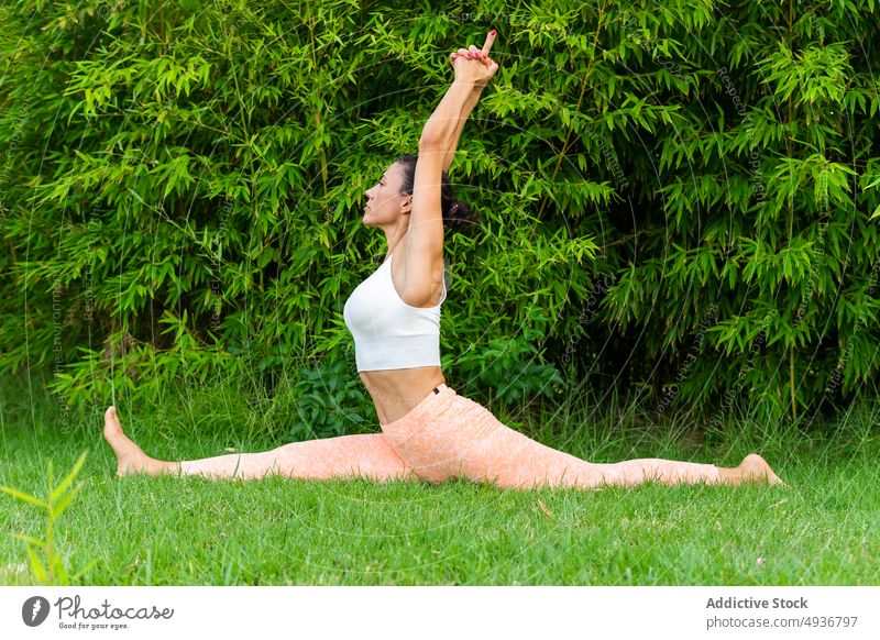 Woman doing Front splits in park woman yoga front splits hanumanasana training exercise practice healthy lifestyle lawn arms raised barefoot grass mindfulness