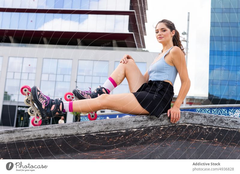Fit young lady in roller blades resting in skate park after training woman city activity self assured summer hobby cool sporty female millennial skirt