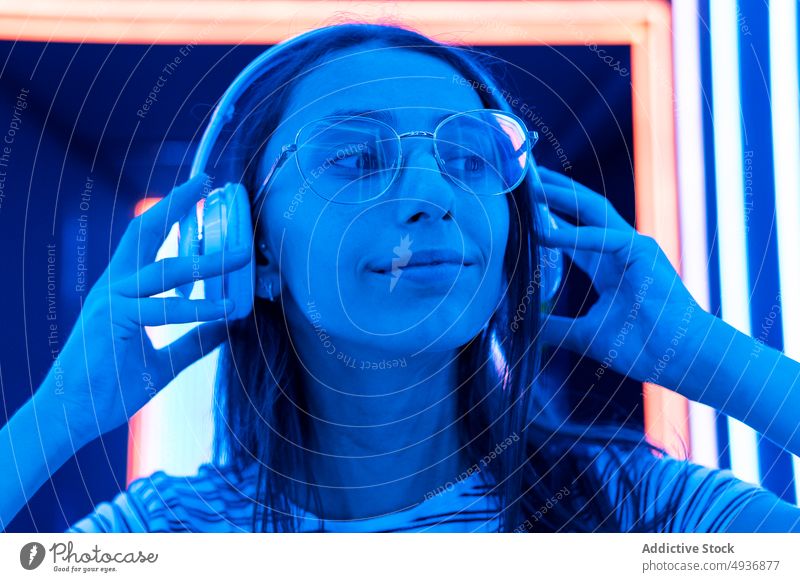 Young female meloman listening to music in futuristic corridor woman illuminate headphones nightlife young sound gadget song audio modern blue neon wireless