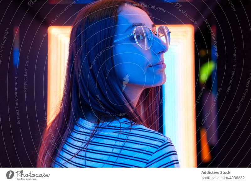 Young woman in nightclub hallway corridor wall blue neon futuristic illuminate colorful female young long hair bright glasses glow modern nightlife luminous