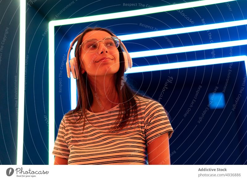 Young female meloman listening to music in futuristic corridor woman illuminate headphones nightlife young sound gadget song audio modern blue orange neon