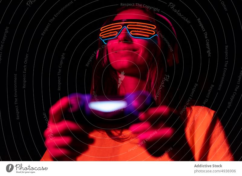 Futuristic young gamer playing at night woman videogame futuristic late gamepad smile red light female modern device gadget control entertain illuminate neon