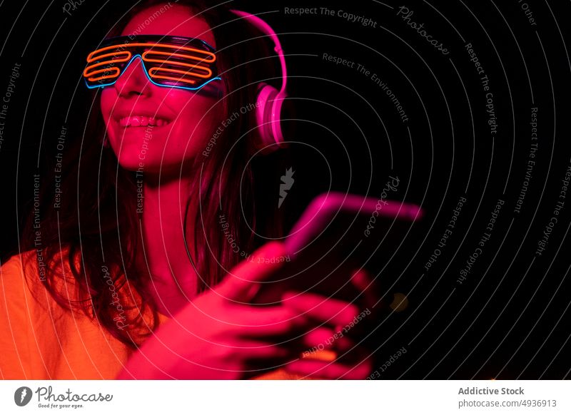 Futuristic meloman using mobile phone woman smartphone texting smile futuristic night listen music red light female young neon illuminate gadget device