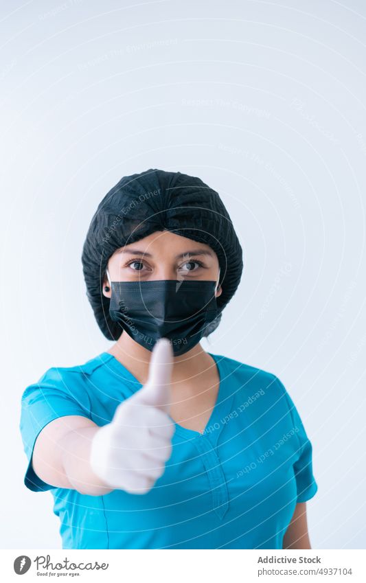 Positive female doctor in uniform sowing like gesture woman thumb up health care medical clinic recommend physician protect prevent young nurse glove cap mask