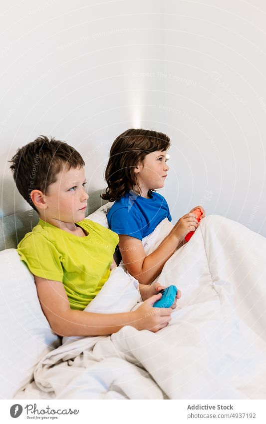Children playing video game in bed children sibling gamepad videogame entertain amusement pastime leisure hobby focused sister concentrated brother boy girl