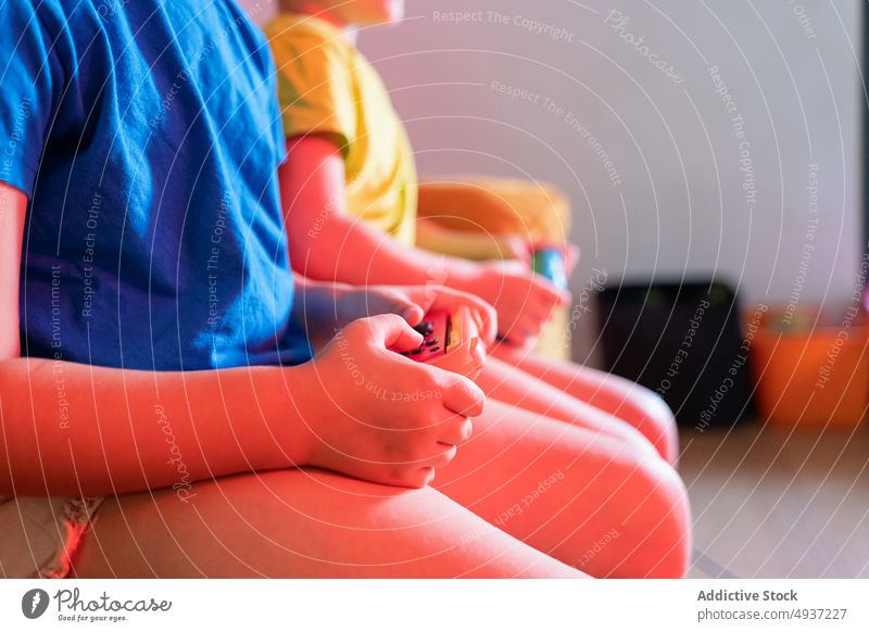 Anonymous children playing video game in evening time sibling living room videogame entertain amusement pastime leisure couch sofa dim neon late hobby hands