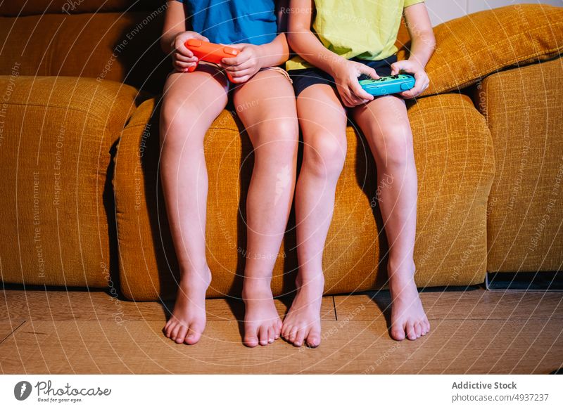 Anonymous children playing video game in evening time sibling living room videogame entertain amusement pastime leisure couch sofa dim neon late barefoot hobby