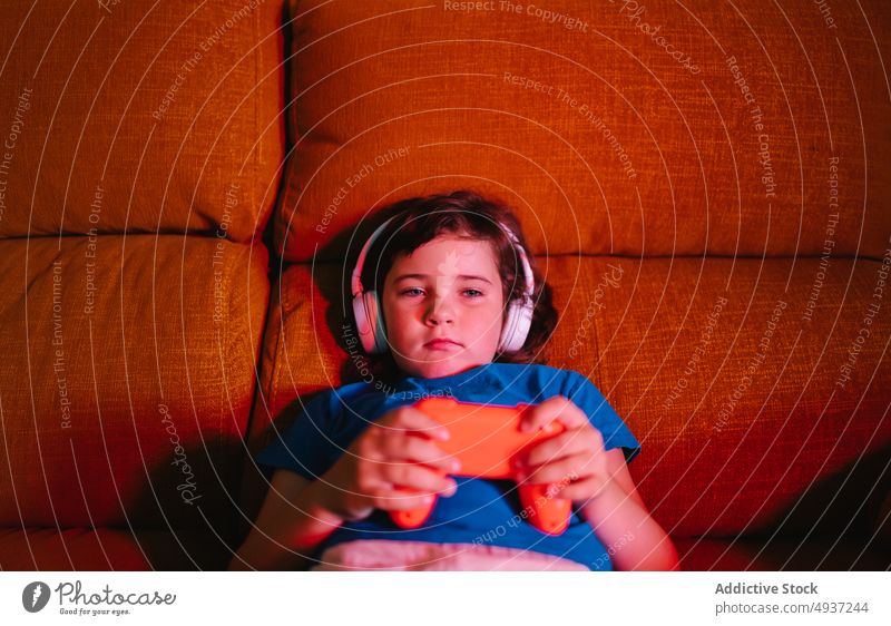 Unhappy girl playing video game in evening time kid living room videogame entertain amusement pastime upset sad unhappy dissatisfied lying down displease