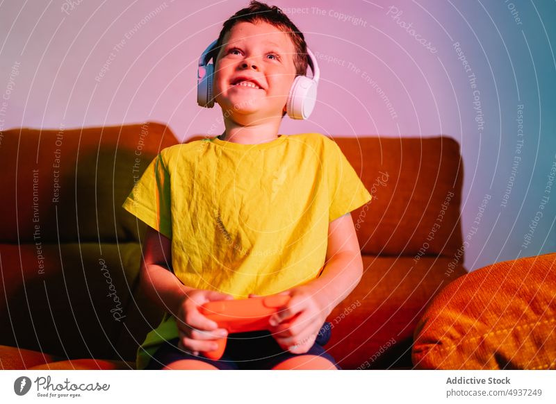 Cheerful boy playing video game kid videogame entertain amusement pastime living room excited happy positive cheerful delight satisfied headphones enjoy leisure