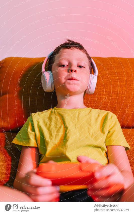 Concentrated boy playing video game kid videogame entertain concentrated amusement pastime focused living room headphones enjoy leisure evening couch sofa hobby