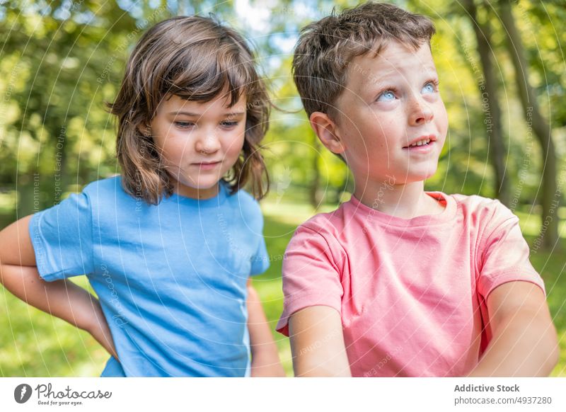 Siblings in sunlit park in summer children sibling weekend together happy sunlight friend smile casual kid glad boy girl hand on waist childhood pastime daytime