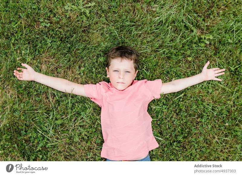 Boy lying on grass looking at camera boy lawn park summer weekend casual child childhood little pastime recreation season field tender individuality nature