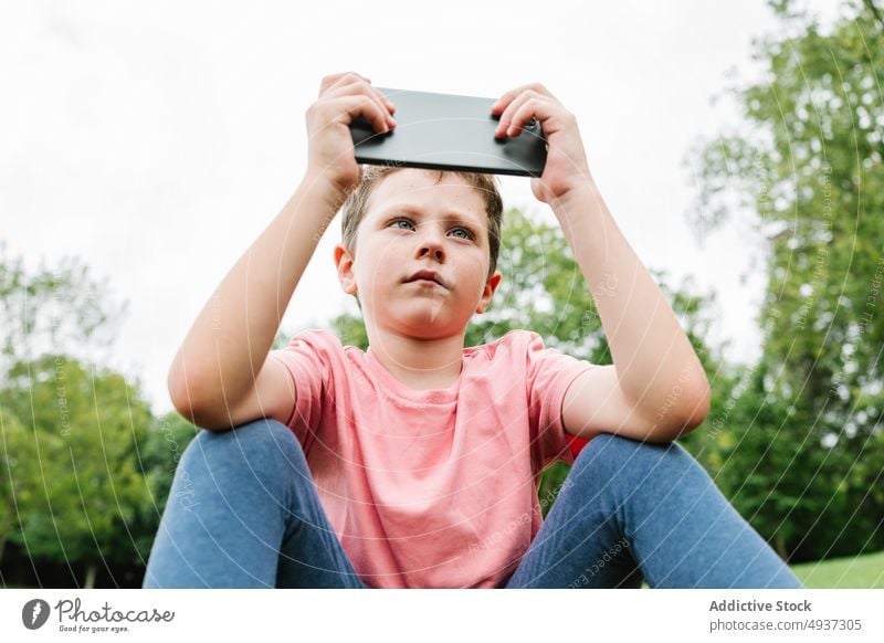 Boy using smartphone on park lawn boy watch video weekend summer pastime child gadget device cellphone grass internet childhood online kid mobile free time