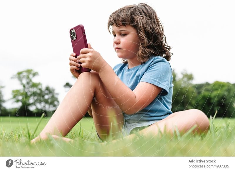 Girl using smartphone on park lawn girl watch video unhappy upset weekend summer pastime child gadget sad device cellphone grass internet childhood angry online