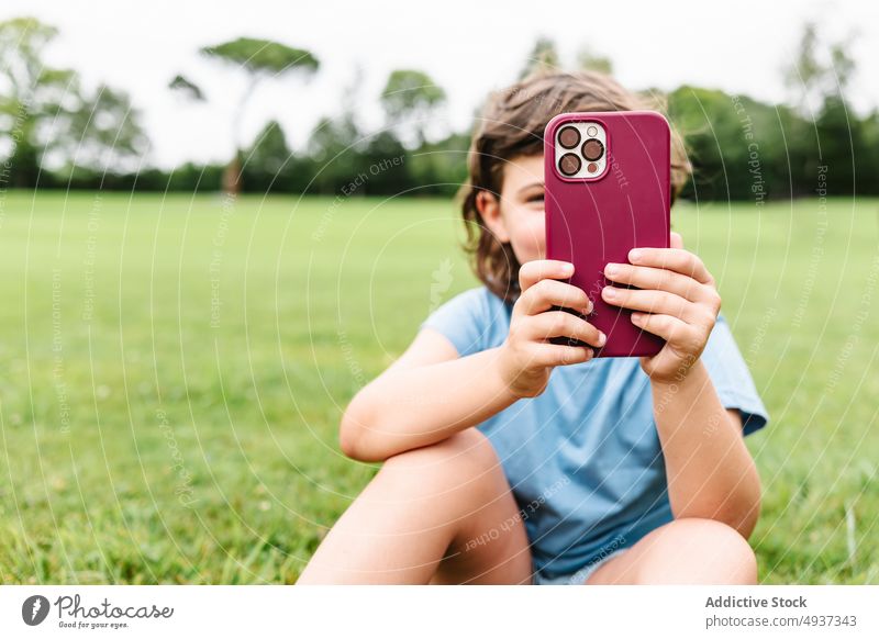Girl using smartphone on park lawn girl watch video weekend summer pastime child gadget device cellphone grass internet childhood online kid mobile free time