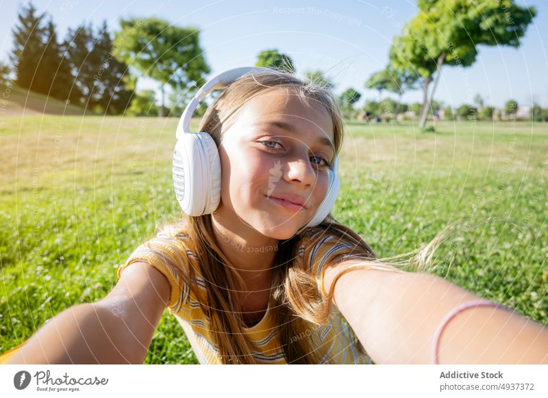 Joyful girl in headphones taking selfie in park teenage smartphone photography social media music listen content carefree moment memory hold self portrait