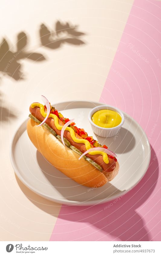 Hot dog in a round plate on white and pink background hot ketchup meal mustard frankfurter lunch meat food snack fast fatty shadow grilled yellow bread