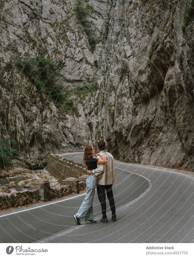 Romantic young couple hugging on road amidst massive rocky cliffs mountain trip traveler together embrace love nature tourist relationship admire boyfriend