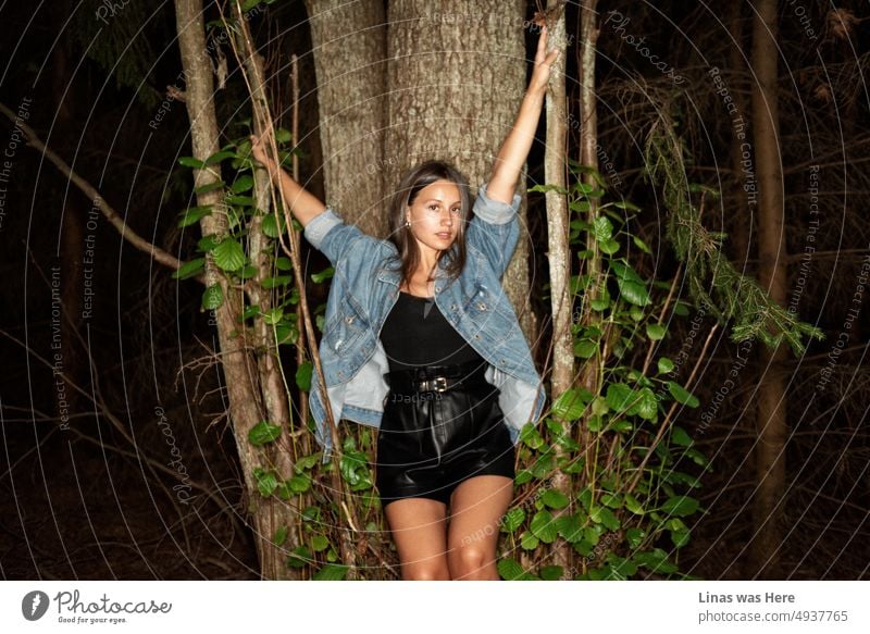 A gorgeous tanned brunette girl getting comfy in the woods. Dressed in blue jeans and black outfit she is looking all gorgeous. Flashlight image makes the image more intimate.
