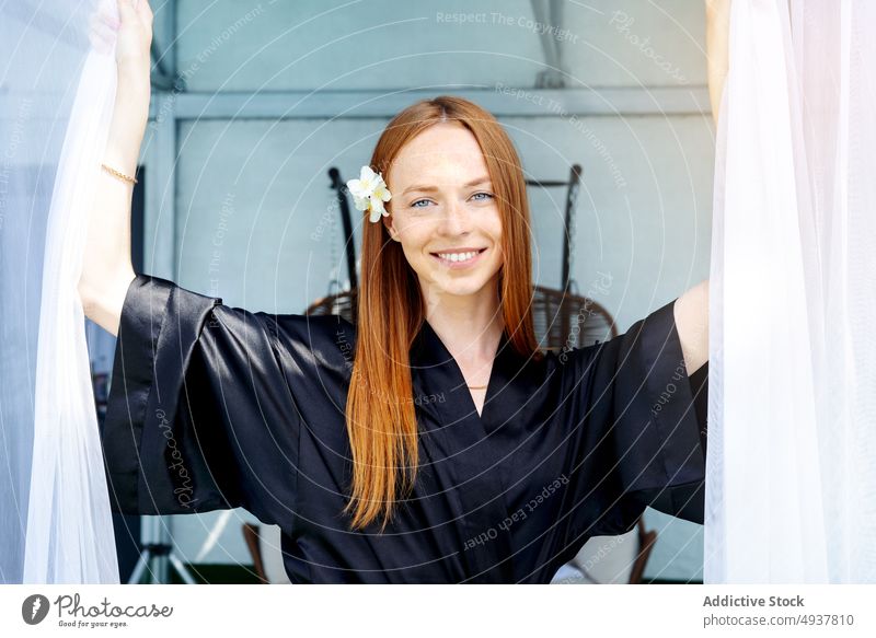 Cheerful redhead woman in spa salon smile client resort curtain rest happy weekend female young pull ginger long hair flower robe silk daytime customer wellness