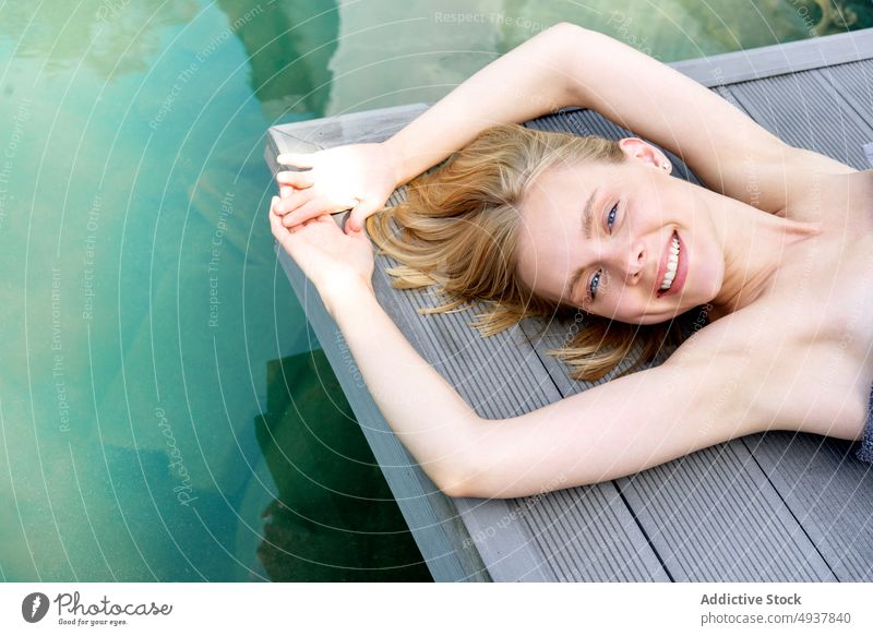 Happy blond woman resting near pool spa resort smile floor water weekend summer female young arms raised clean relax positive chill hotel happy cheerful glad