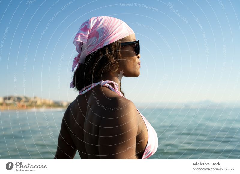 Black female tourist admiring sea woman admire weekend resort summer blue sky water vacation black african american ethnic bra swimwear headscarf sunglasses