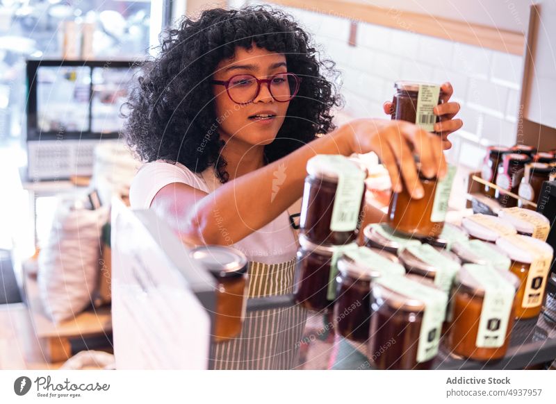 Black woman arranging jam sauces on shelf in shop grocery arrange work eco friendly small business jar female young black african american ethnic glasses