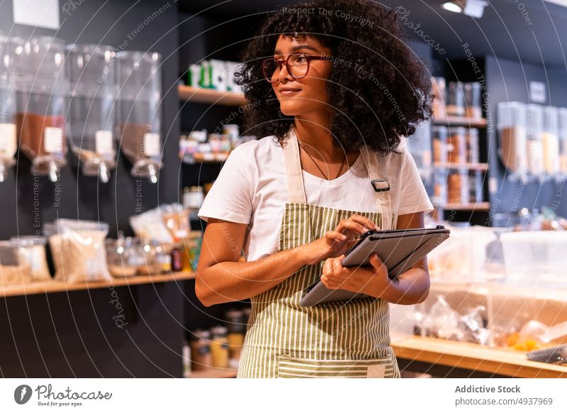 African American woman checking goods in grocery shop vendor pasta store zero waste container tablet female young black african american ethnic inventory