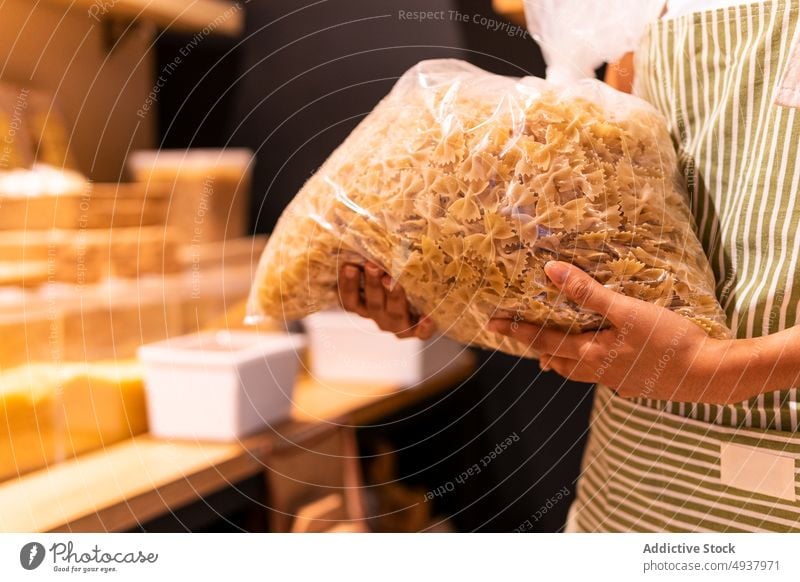 Crop woman with bag of pasta vendor carry work grocery farfalle shop food female uniform apron organic store package product job sustainable service raw plastic
