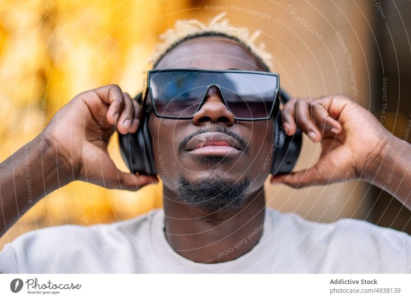 Black man listening to music on street urban meloman happy headphones adjust male young black african american sunglasses ethnic enjoy wireless t shirt sound
