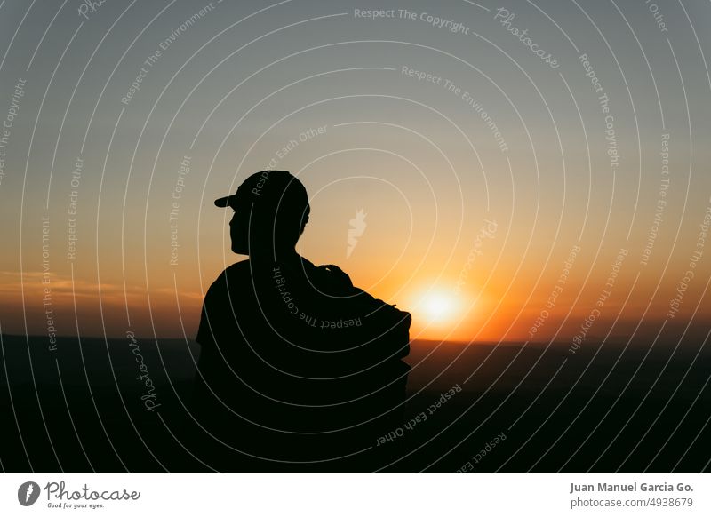 Silhouette of man with cap and backpack contemplating the landscape in the orange light of sunset therapy teen experiences adventure achievement bivouac