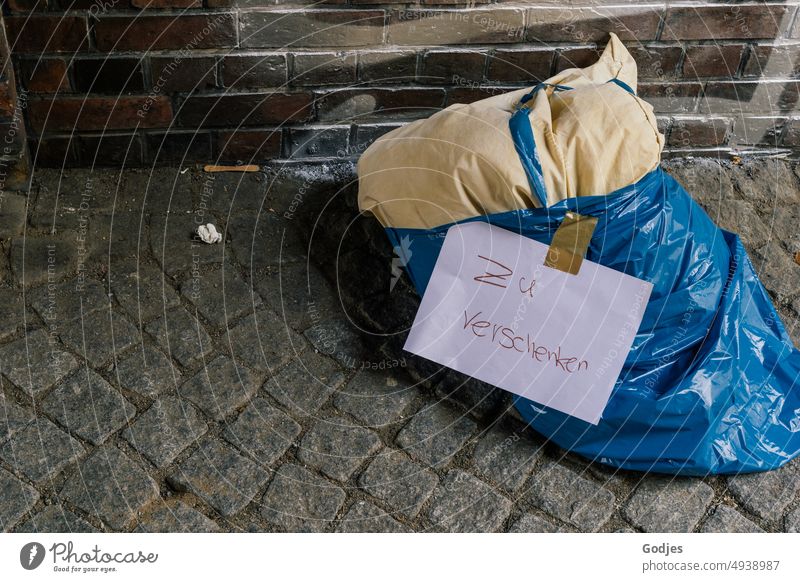 Pillow in a garbage bag lies on the side of the road with the inscription 'to give away objects Homelessness Gift Street Ground background context needy Junk