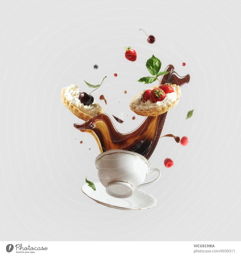 Creative levitation food concept with flying coffee splashing in cup and cakes with various berry and fruits at light background. creative liquid motion