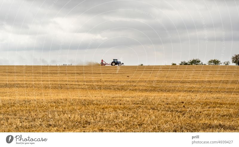 Tractor on a stubble field tractor traction engine agriculture rural farming farmland cultivating summer stormy clouded overcast plantation Hohenlohe germany