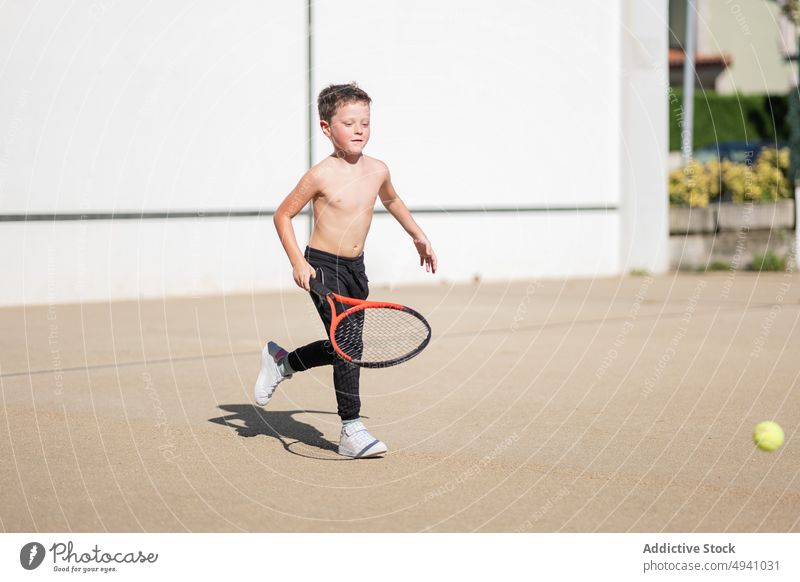 Shirtless boy playing tennis on street weekend game happy racket summer child daytime sport activity kid shirtless childhood ball exercise hobby pastime