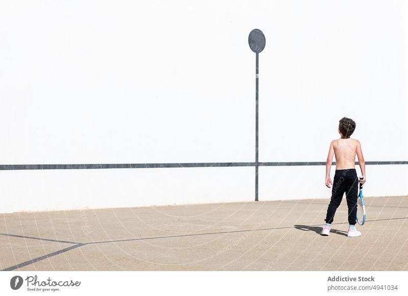 Anonymous shirtless boy playing tennis on street weekend game racket summer child daytime activity kid childhood hobby pastime carefree lifestyle sunlit