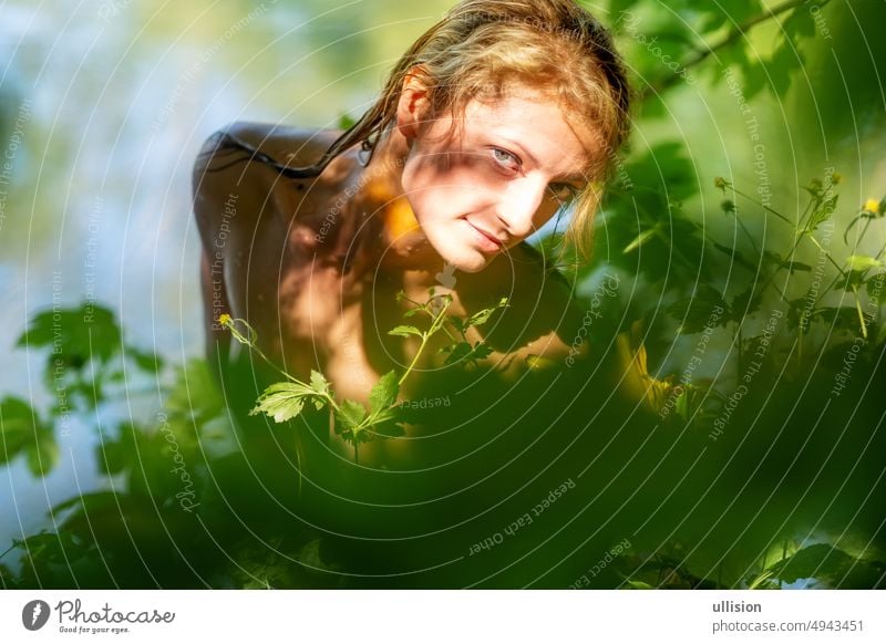 Beautiful young sexy naked nude woman girl, with wet blonde hair, looks out between green yellow leaves, at a sunny summer lake beautiful copy space slavic