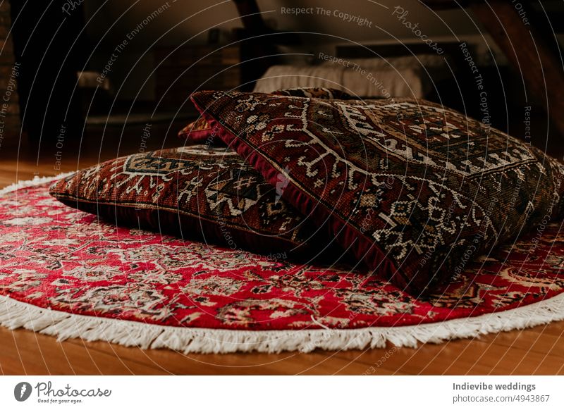 Two red persian bed pillows on a round hand knitted rug on the floor. Home decoration detail, copy space. Colorful carpet and textile. antique arabic asian