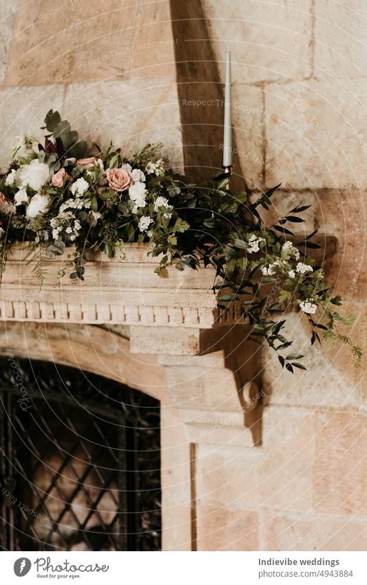 A beutiful flower decoration on top of a sandstone fireplace lintel. Copy space. Wedding interior decoration concept. White roses, candle and green flowers. Cast iron protection mesh in the fireplace.